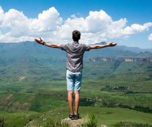 man with arms raised looking at clouds and mountain